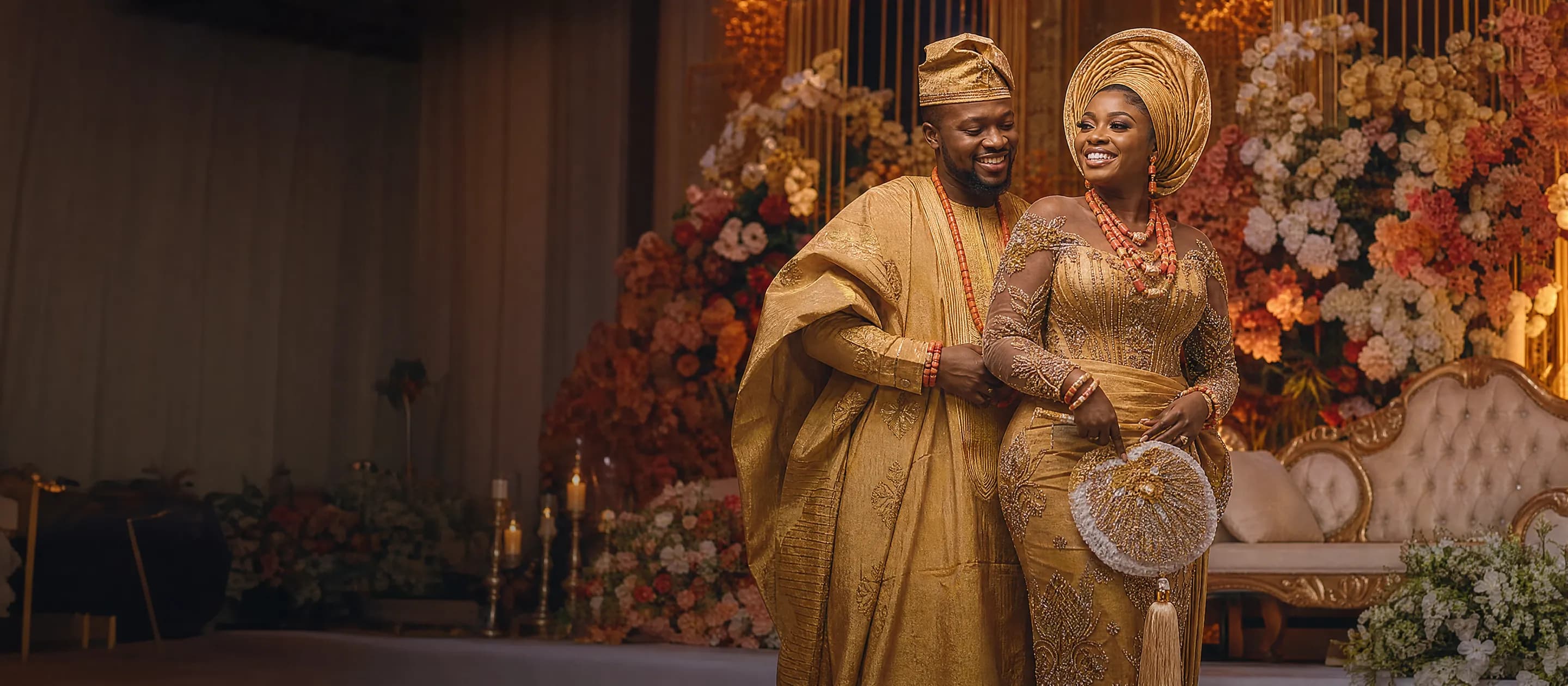 Regal West African couple in gele and agbada on a floral stage